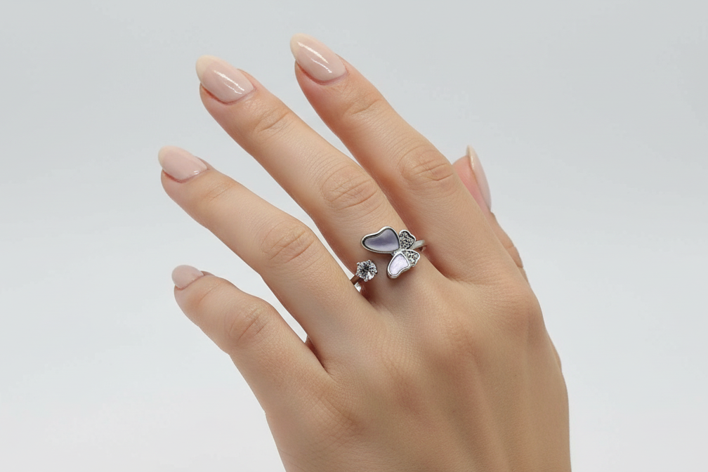 Hand wearing a silver ring with a heart-shaped gemstone on a light gray background