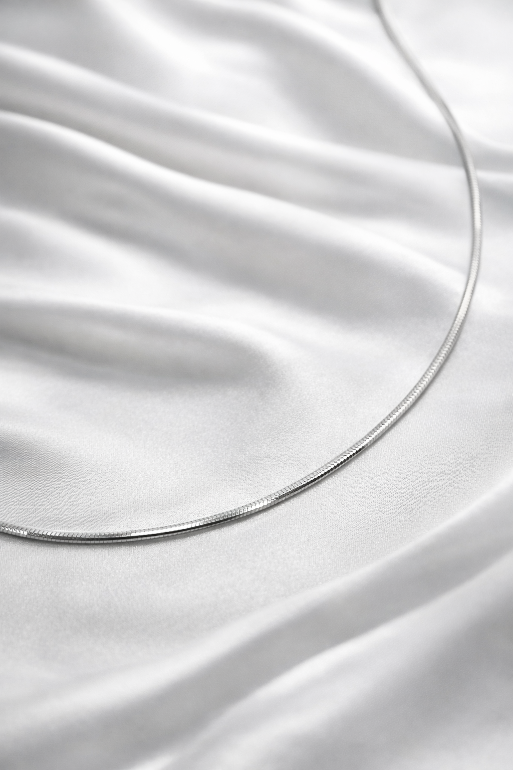 Close-up of a silver necklace on white satin fabric