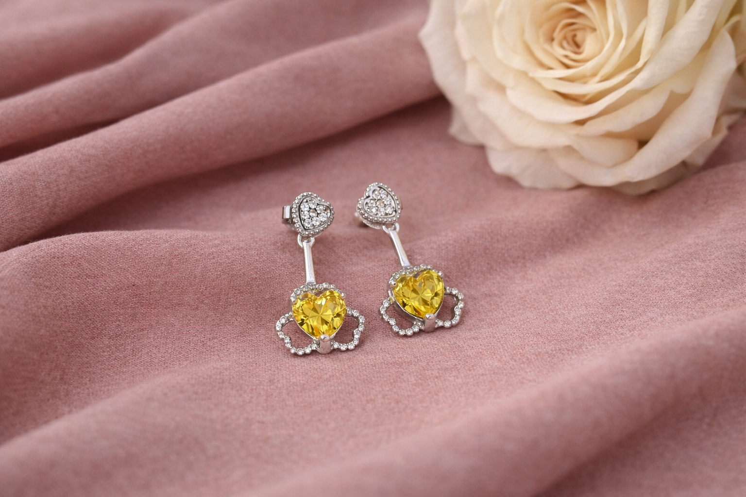Pair of yellow gemstone earrings on a pink fabric background with a white rose.
