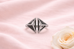 Silver ring with geometric design on a pink satin background with a white rose.