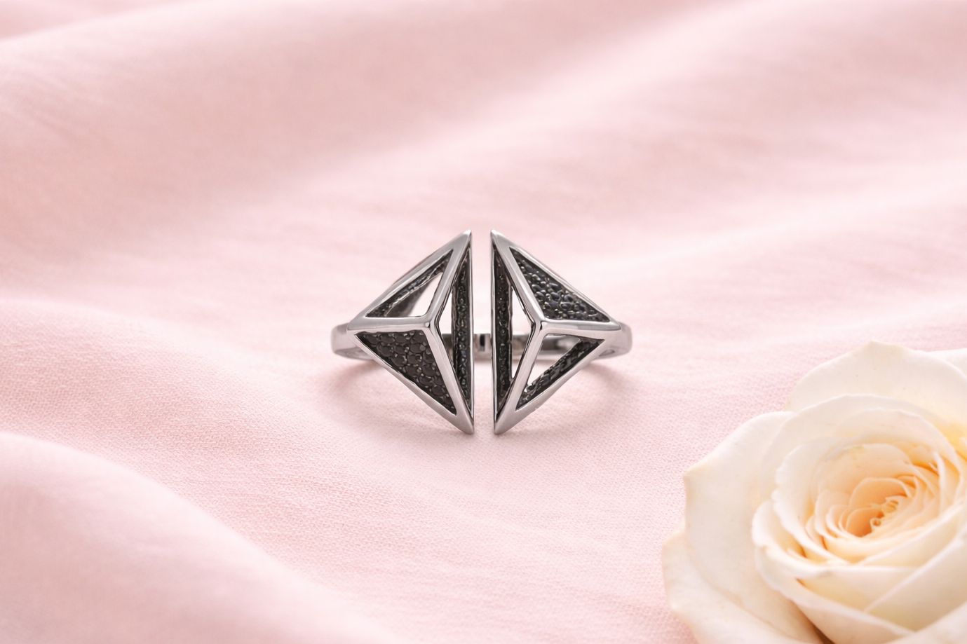 Silver ring with geometric design on a pink satin background with a white rose.