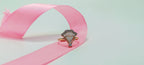 Diamond ring on a pink ribbon against a light green background