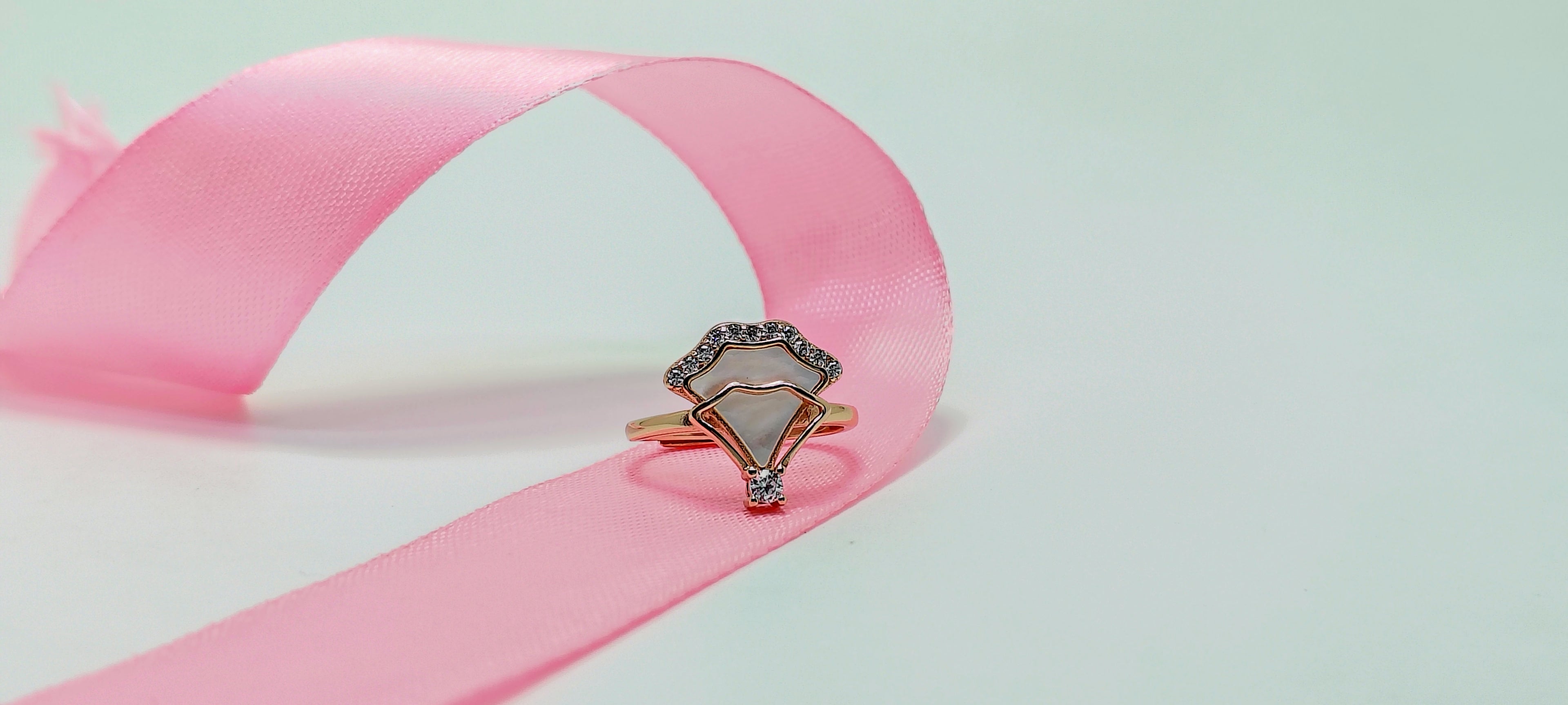 Diamond ring on a pink ribbon against a light green background
