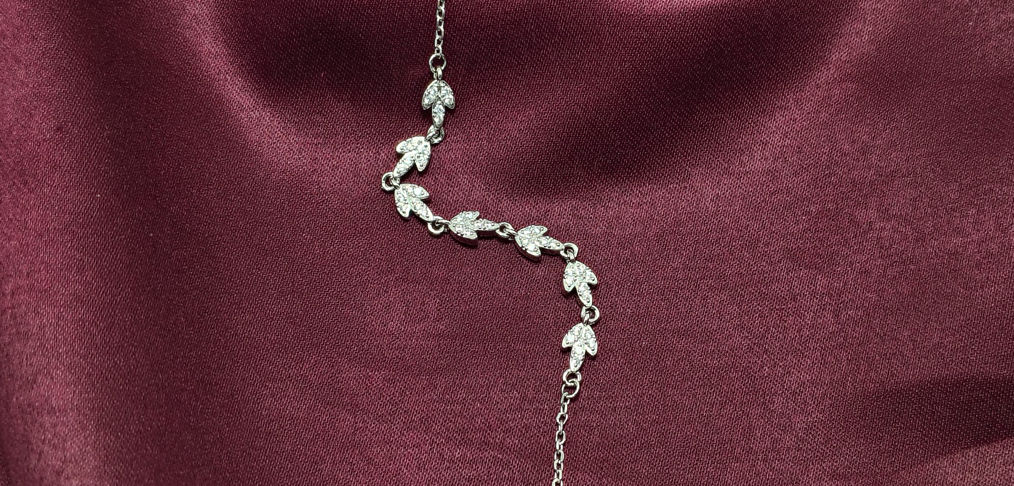 Silver necklace with leaf designs on a burgundy fabric background