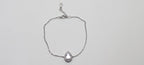 Silver bracelet with a teardrop-shaped charm on a light gray background
